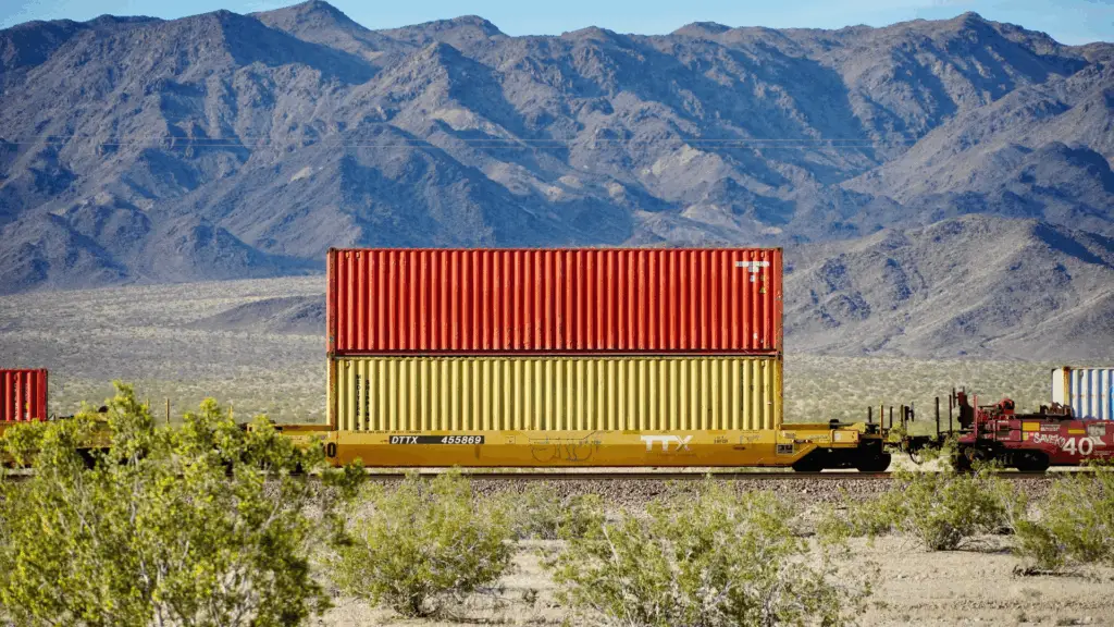 Rail freight shipment with stacked shipping containers traveling through the desert